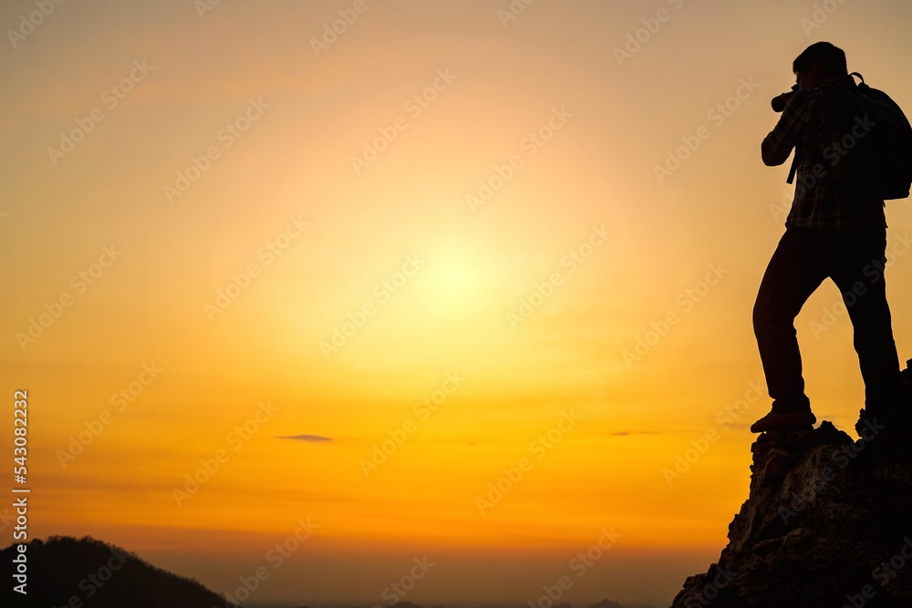 A silhouette of a photographer standing at the top of a mountain in the evening photographing the sunset.Concept of photographer and adventure travel photography A silhouette of a photographer standing at the top of a mountain in the evening photographing the sunset.Concept of photographer and adventure travel photography