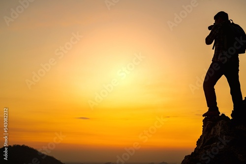 A silhouette of a photographer standing at the top of a mountain in the evening photographing the sunset.Concept of photographer and adventure travel photography