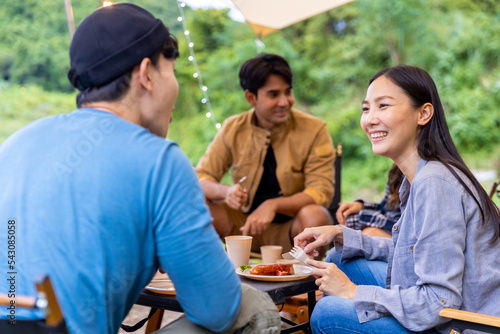 Group of Happy Asian people enjoy and fun outdoor lifestyle camping together on holiday travel vacation. Man and woman friends playing guitar and singing together while having dinner at summer night.