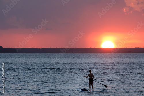 A woman rides a stand-up paddleboard at sunset © brianeden