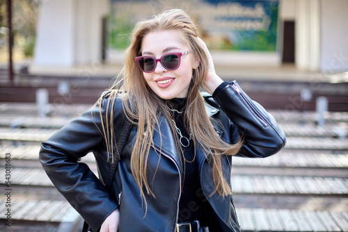 Outdoor portrait of a smiling girl in a black jacket and pink sunglasses