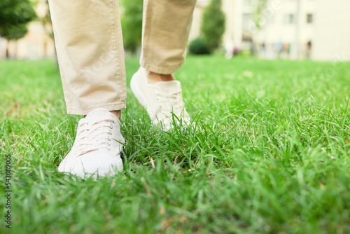 Man in stylish sneakers walking on green grass outdoors, closeup