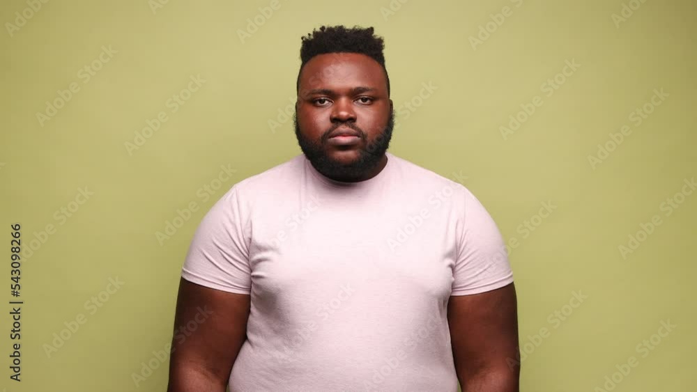 Attractive serious strict African-american man wearing pink t-shirt standing looking at camera with bossy facial expression, being in bad mood. Indoor studio shot isolated on light green background. Attractive serious strict African-american man wearing pink t-shirt standing looking at camera with bossy facial expression, being in bad mood. Indoor studio shot isolated on light green background.