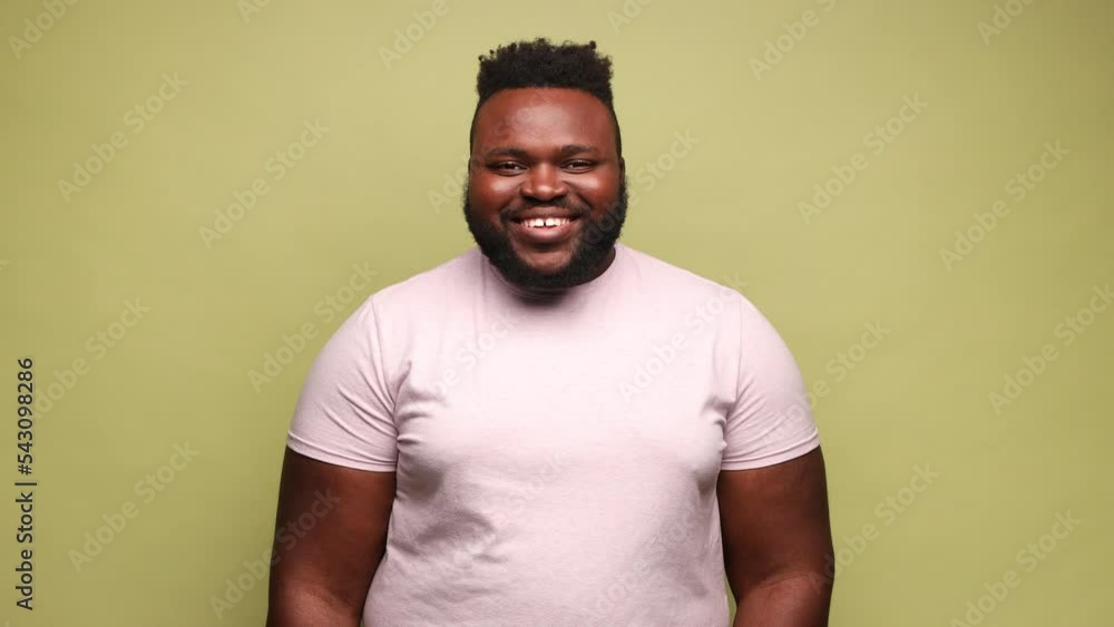 Handsome smiling african-american man wearing pink t-shirt looking at camera, expressing positive emotions, being in good mood. Indoor studio shot isolated on light green background. Handsome smiling african-american man wearing pink t-shirt looking at camera, expressing positive emotions, being in good mood. Indoor studio shot isolated on light green background.