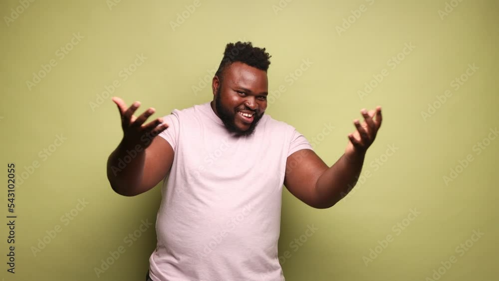 Bearded African-american man wearing pink t-shirt with generous smile widely spreading his arms welcoming dear guests, greeting. Indoor studio shot isolated on light green background. Bearded African-american man wearing pink t-shirt with generous smile widely spreading his arms welcoming dear guests, greeting. Indoor studio shot isolated on light green background.