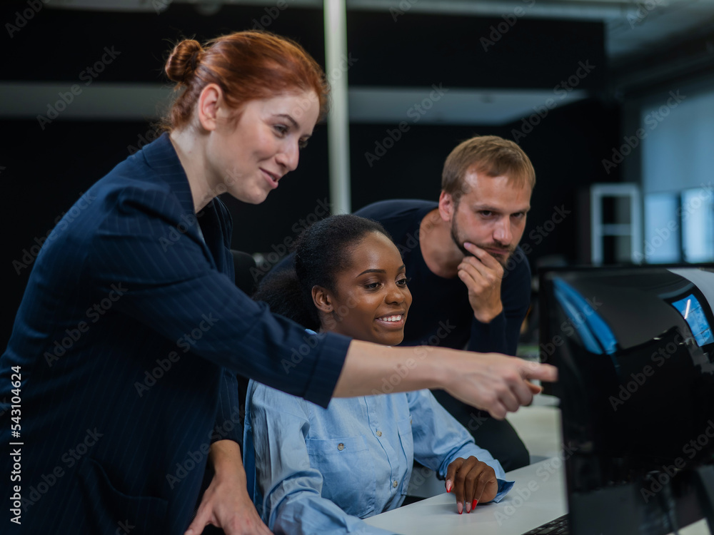 Obraz premium Colleagues look at the monitor and decide working moments. African young woman, caucasian man and red-haired caucasian woman communicate in the office. 