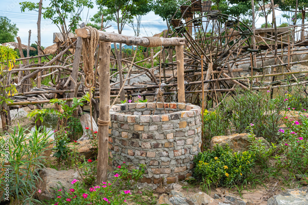 Beautiful artesian well made by bricks with cement and wheel pulley with metal bucket and rope in peaceful garden atmosphere. Retro stone water well in rural area.Garden decoration with antique items Beautiful artesian well made by bricks with cement and wheel pulley with metal bucket and rope in peaceful garden atmosphere. Retro stone water well in rural area.Garden decoration with antique items