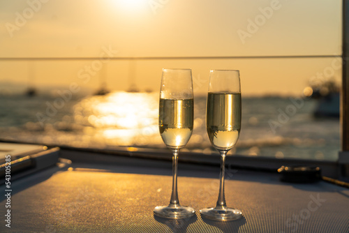 Champagne in the glass on tray for serving to passenger tourist on luxury catamaran boat yacht sailing in the ocean at summer sunset. Summer travel vacation trip and celebration holiday event concept