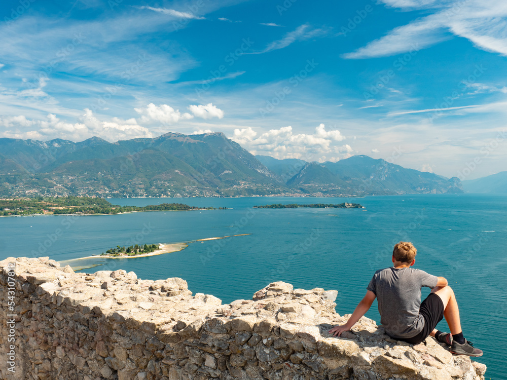 Boy sit  alone on rest of Manerba castle wall above Lago di Garda lake