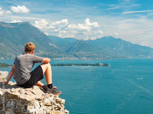 Teenager with sports body resting on rough stony wall above lake photo