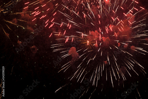 Bright fireworks with red sparks and smoke flying against the background of the night sky. Beautiful colorful festive fireworks against the black sky, long exposure