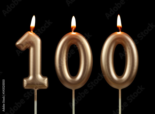Burning gold birthday candles isolated on black background, number 100