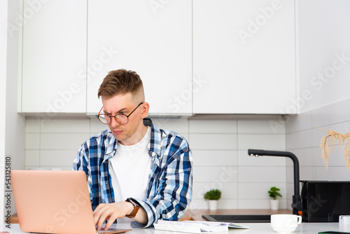 A man in a plaid shirt and glasses works on a laptop with a surprised face. Freelancer works from home.