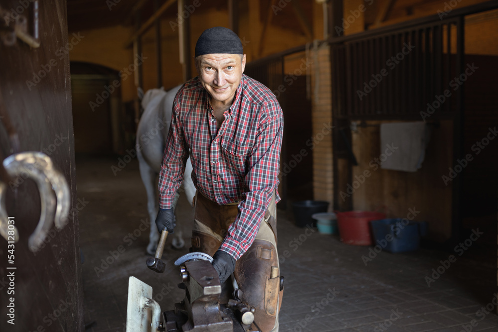 happy European blacksmith working on iron horseshoe with hammer happy European blacksmith working on iron horseshoe with hammer