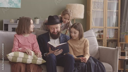 Jewish man reading the Tanakh to his three daughters on Hanukkah, celebrating at home photo