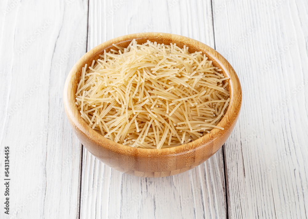 Uncooked filini pasta in wooden bowl on white wooden background