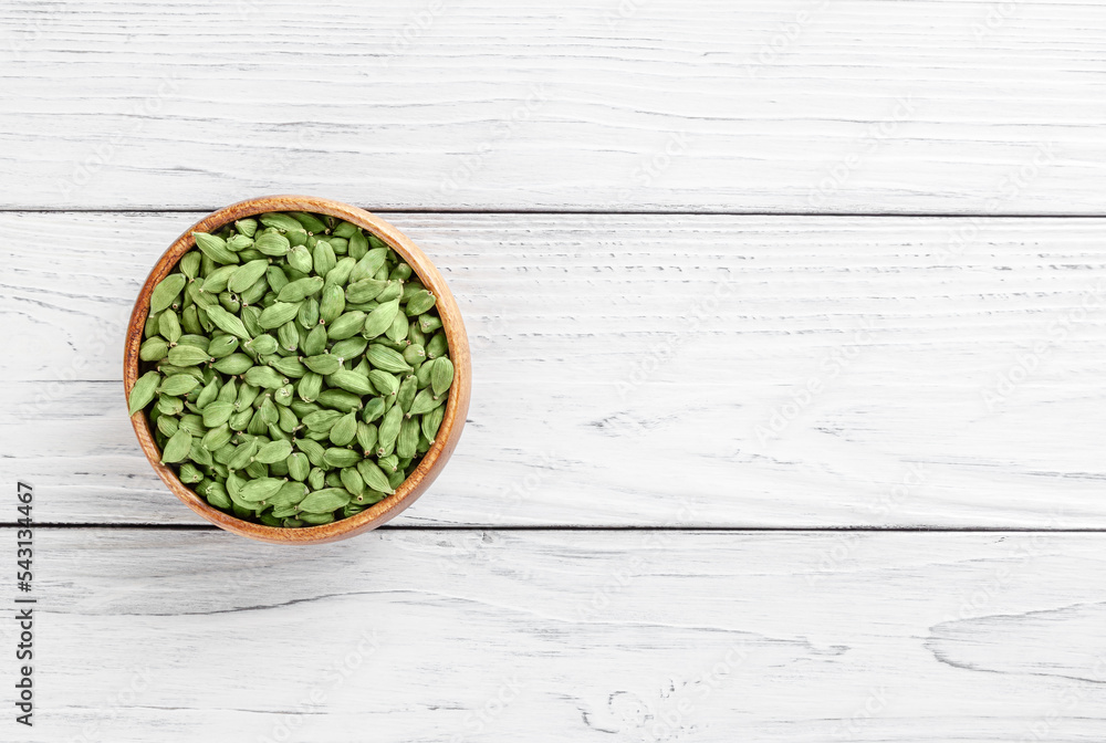 Cardamom pod in wooden bowl on white wooden background with copy spase