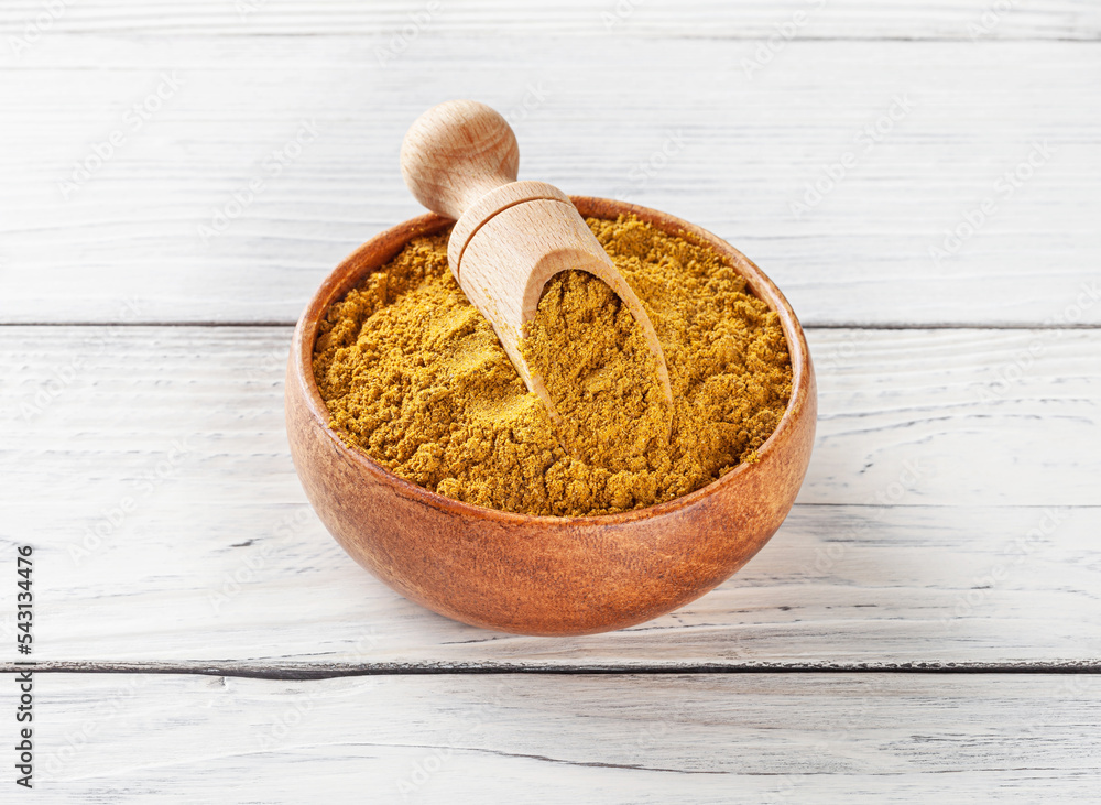 Curry powder in wooden bowl with scoop on white wooden background