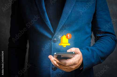 push notification. Businessman holding smartphone with virtual yellow bell ringing for application notification alert concept.