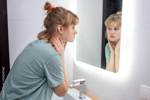Teen girl looks in the mirror at problem skin