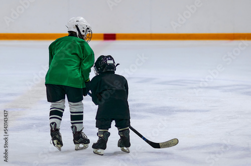 Canvas Print Two boys in hockey uniforms and protective helmets with hockey skates and a hockey stick standing on the ice of a large ice arena