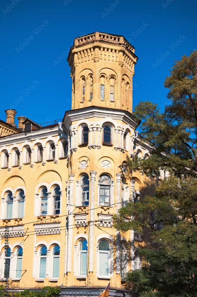 A low angle landscape view of vintage yellow brick building with the tower against blue sky. Neo-gothic style architecture