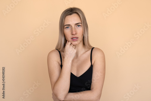 Portrait of the sad young woman thinking about relationships personal problems, standing over beige background. Upset girl lost in thoughts feel lonely depressed pondering or mourning