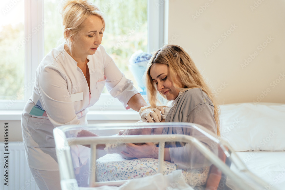 Obraz premium View of a doctor helping a new mother feed the baby with a breast. Mom breastfeeding newborn baby in hospital ward. Breastfeeding consultant help her.