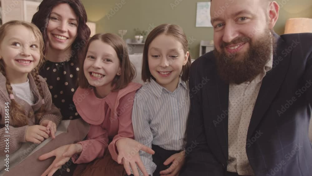 Handheld POV slowmo of Jewish man recording video of himself with his wife and three happy elementary school daughters waving and smiling at camera sitting on couch at home Handheld POV slowmo of Jewish man recording video of himself with his wife and three happy elementary school daughters waving and smiling at camera sitting on couch at home