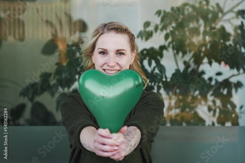 smiling young vegan girl full of joy holding a green heart air balloon in her hand for more environmentally friendly awareness to care about planet earth against climate change 