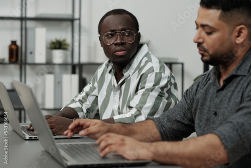 Fotografija Young African American man in casual shirt looking at colleague of another ethni