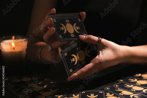 Soothsayer shuffling tarot cards at table in darkness. Fortune telling photo