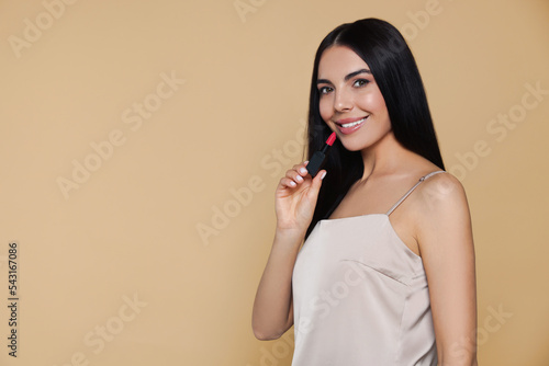 Young woman with beautiful makeup holding nude lipstick on beige background, space for text