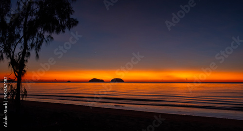 Sunrise on Cowley Beach, Queensland, Australia. There is a tree and sand in the foreground with two island on the horizon. photo