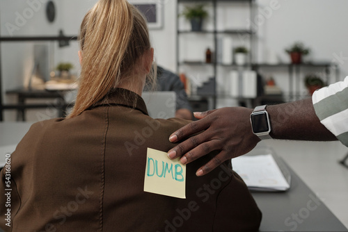 Valokuva African American businessman putting sticker with word dumb on back of blond fem