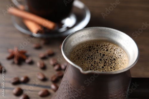 Turkish coffee in cezve on wooden table, closeup. Space for text photo