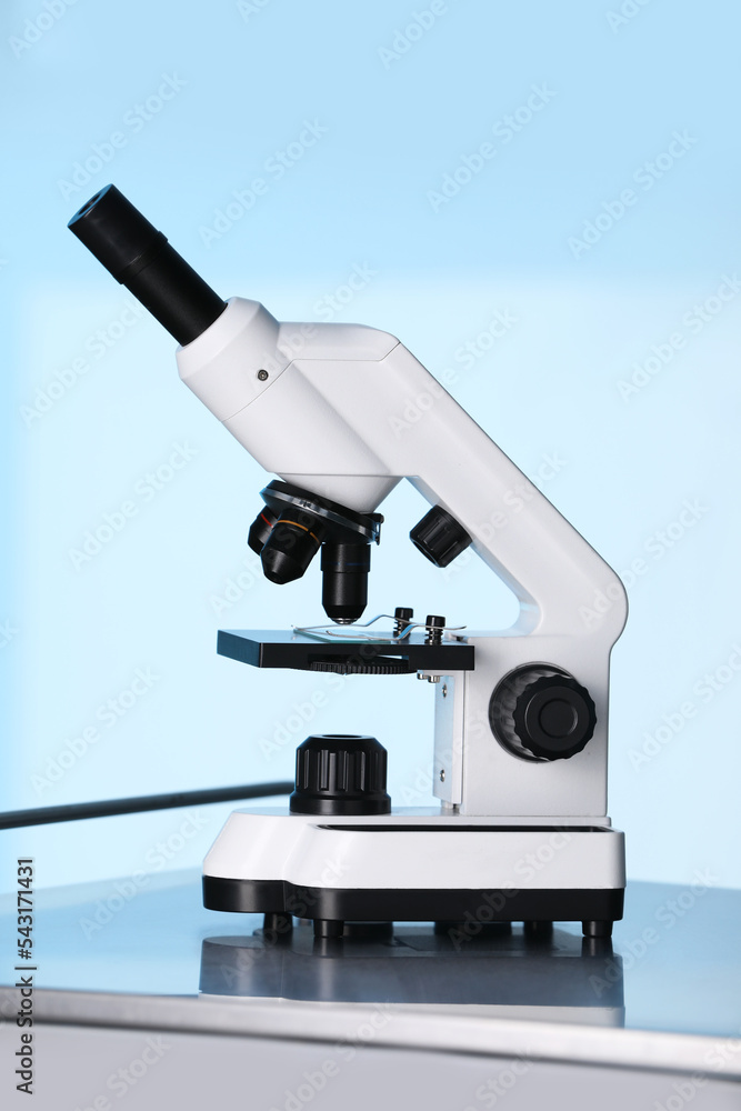 Modern microscope on metal table against light blue background