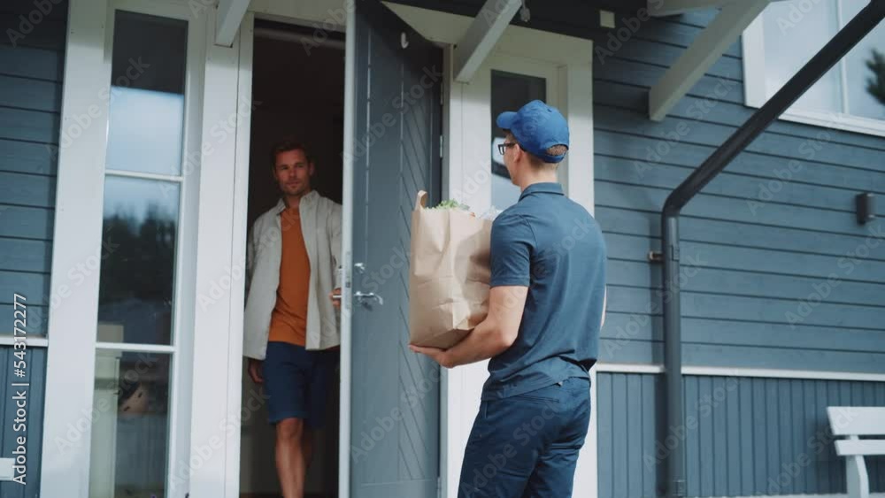 Young Man Working in a Grocery Delivery Service, Bringing a Brown Paper Bag Full of Fresh Vegetables and Other Food Items to a Residential Area Home. Happy Addressee Opens the Door and Signs a POD. Young Man Working in a Grocery Delivery Service, Bringing a Brown Paper Bag Full of Fresh Vegetables and Other Food Items to a Residential Area Home. Happy Addressee Opens the Door and Signs a POD.