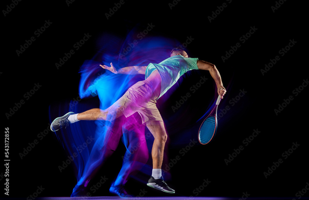 Young male tennis player in t-shirt and shorts playing tennis isolated over dark background in mixed purple neon light. Competition, creativity, art, ad Young male tennis player in t-shirt and shorts playing tennis isolated over dark background in mixed purple neon light. Competition, creativity, art, ad