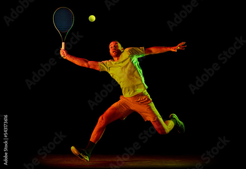 Studio shot of professional tennis player playing tennis isolated over dark background in neon light. Concept of motion, speed, professional sport. © master1305