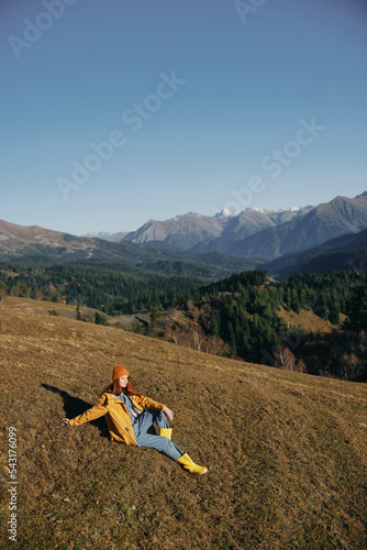 Woman sitting full-length on a hill and looking out over the mountains happy nature trip on a hike in the autumn