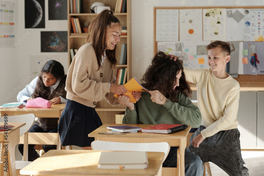 Two cruel classmates fighting with schoolboy, mocking at him and taking his copybook against African American schoolgirl making notes Two cruel classmates fighting with schoolboy, mocking at him and taking his copybook against African American schoolgirl making notes