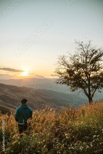 Travel tourist alone Hiking adventure. Young man standing on top of cliff in summer mountains with sunset enjoy view nature cliff mountain
