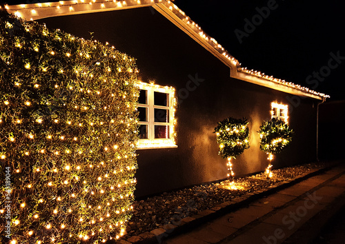 Danish home decorated with christmas lights glowing outside the house and in the garden in a December night