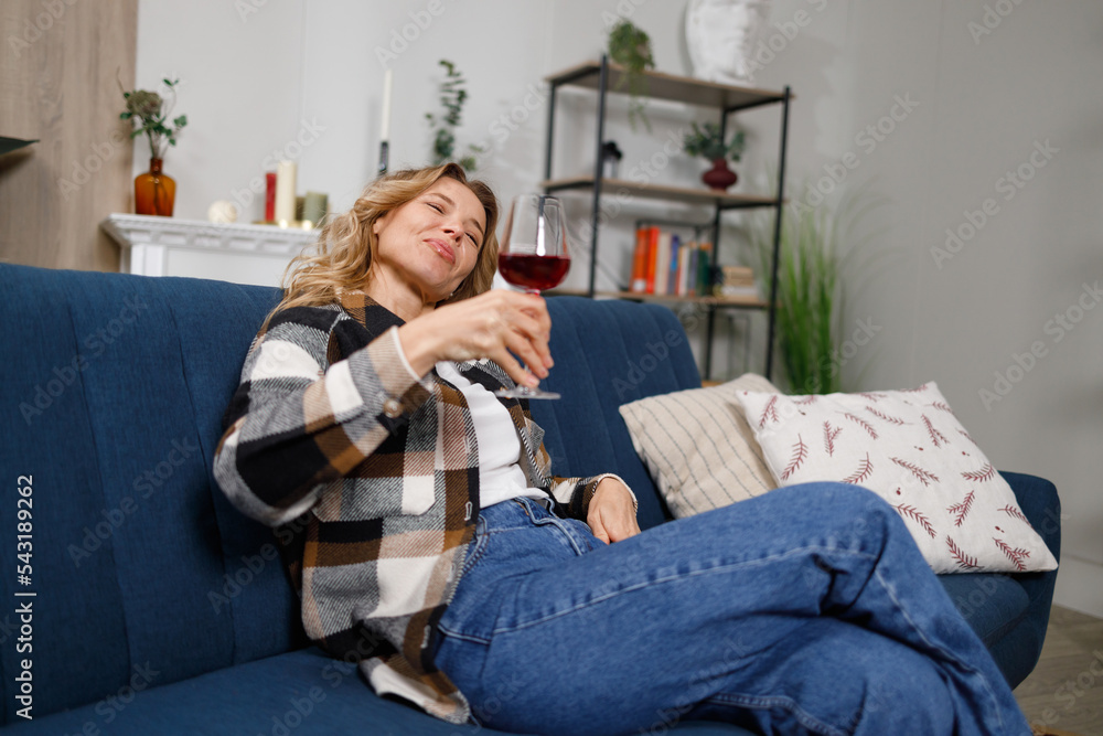 Drunk middle-aged woman with glass of red wine on sofa at home Drunk middle-aged woman with glass of red wine on sofa at home