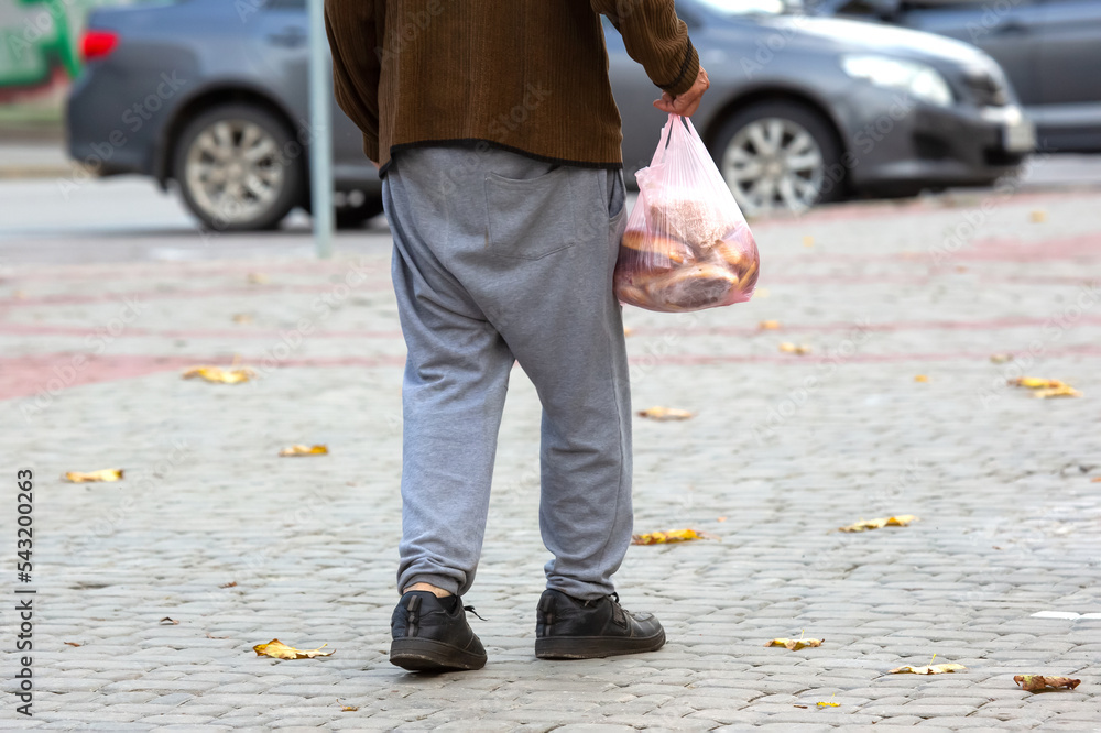 Obraz premium homeless poor man walks down the city street with a bag in his hand. social problems of the city and people