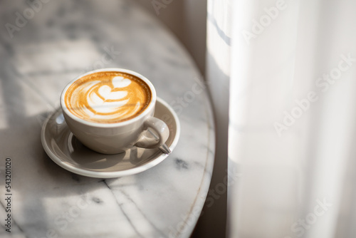 A cup of latte on a marble table in the cafe  beautifully illuminated by the window light.