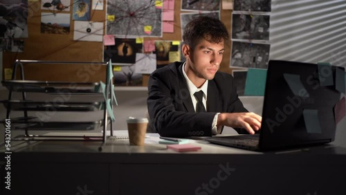 Detective processing evidence in office, working at desk using laptop photo
