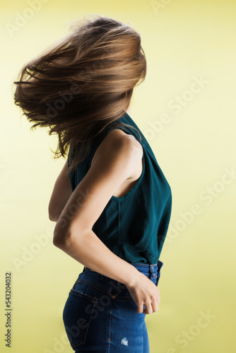 Beautiful girl with flowing hair against yellow background. Brunette lady with fancy shirt and jeans posing in studio... photo