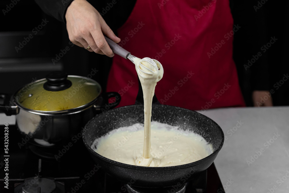 Chef cook making white cheese sauce for mac and cheese meal. Ingredients: Milk, cheese, flour and butter in wok pan on kitchen gas stove. Chef cook making white cheese sauce for mac and cheese meal. Ingredients: Milk, cheese, flour and butter in wok pan on kitchen gas stove.
